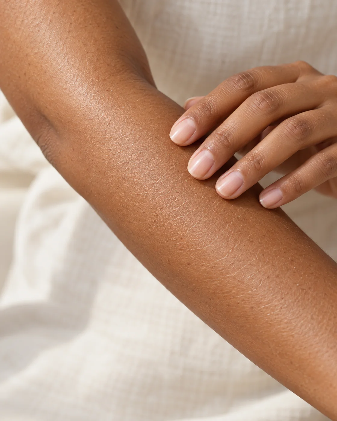 Main adulte touchant légèrement un avant-bras avec de fines marques naturelles de sécheresse, sans pincer la peau